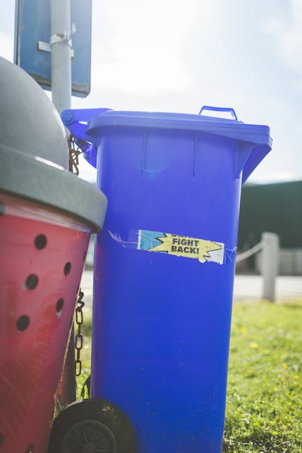 A white disposable paper cup lies on its side on a stone or brick pavement, with part of the cup's printed design visible. The background shows a blurred outdoor setting, possibly a pathway or entranc