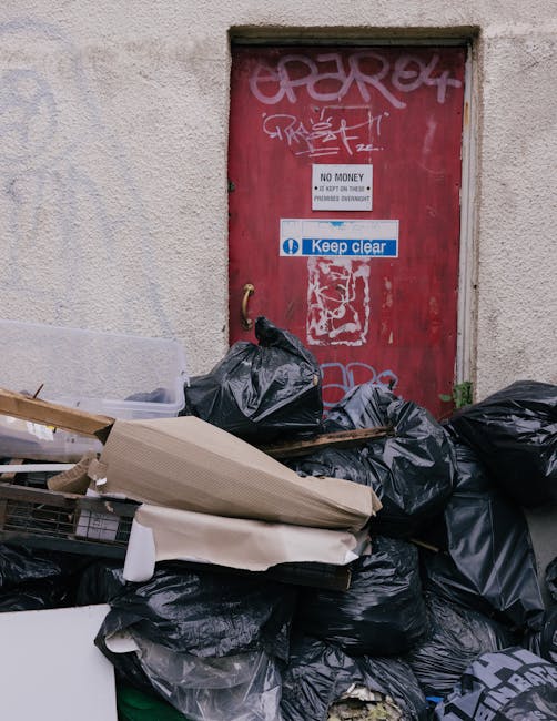 A white panel van parked on a city street immediately adjacent to a multi-storey building with a pale façade featuring vertical architectural details and multiple rectangular windows. The van’s sli